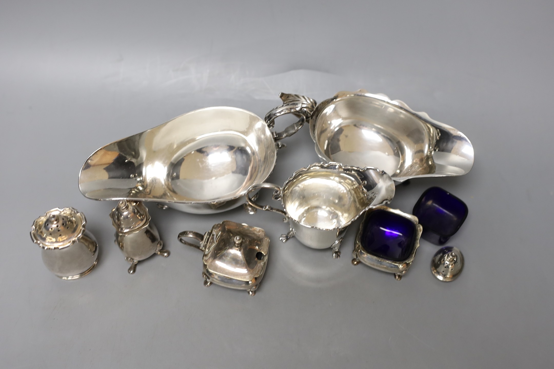 Two George V silver sauceboats, one a.f., a silver cream jug, four silver condiments, a lid and blue glass liner.